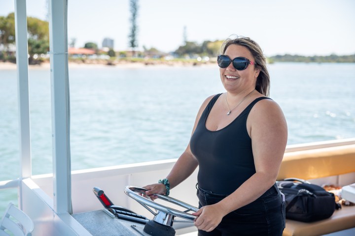 a woman standing in front of a boat next to a body of water