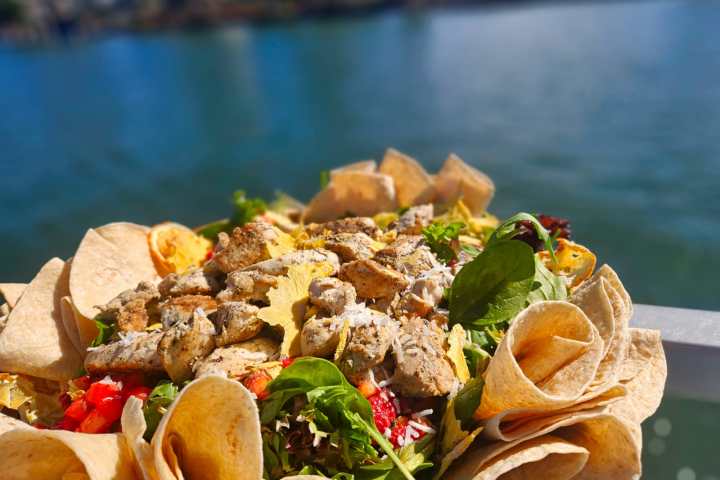 Salad with grilled chicken and tortilla chips by a lakeside.