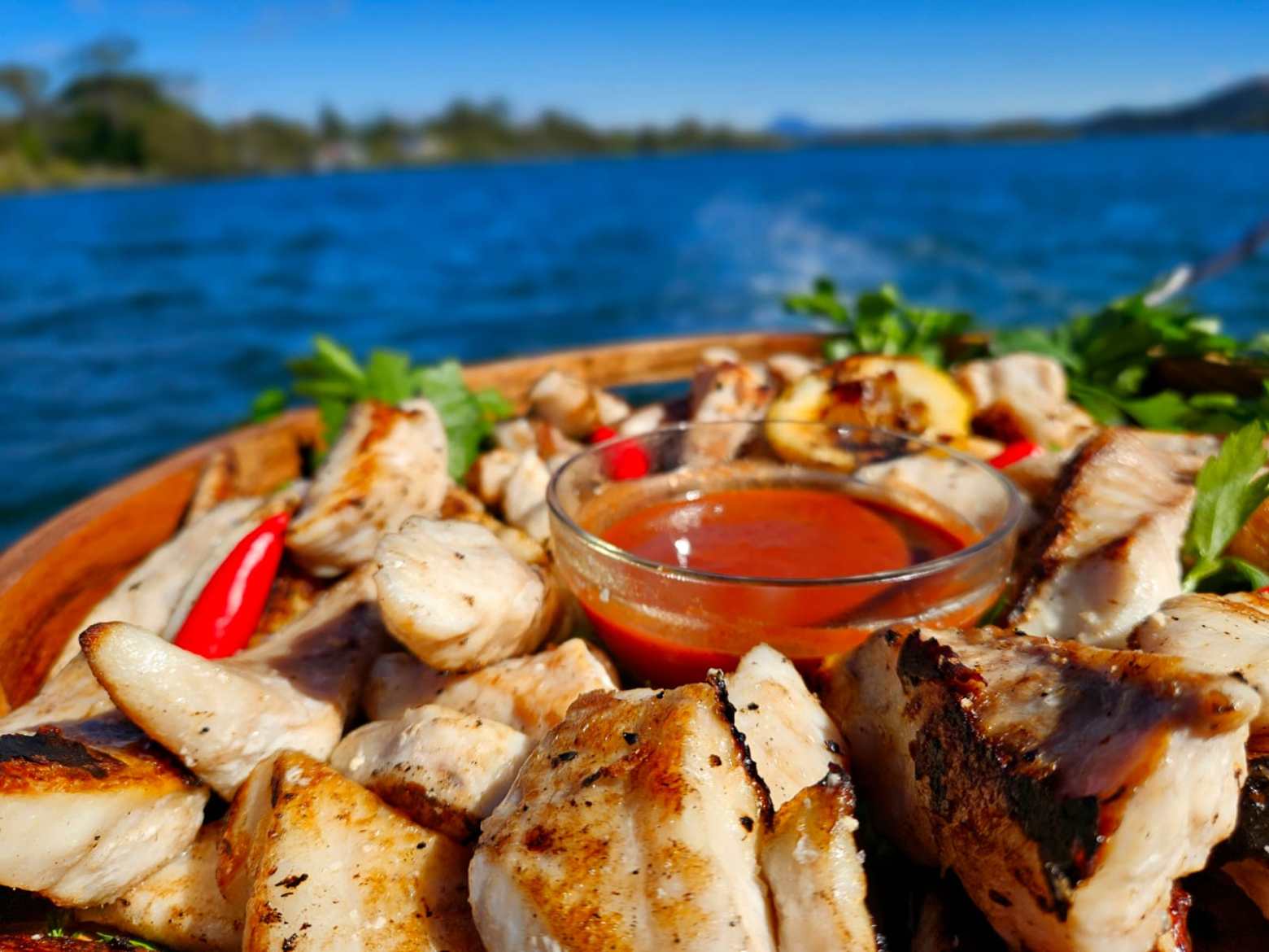 Grilled chicken and red sauce in a dish with a lake view background.