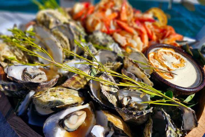 Platter of oysters and prawns with herbs and sauce bowl on display.