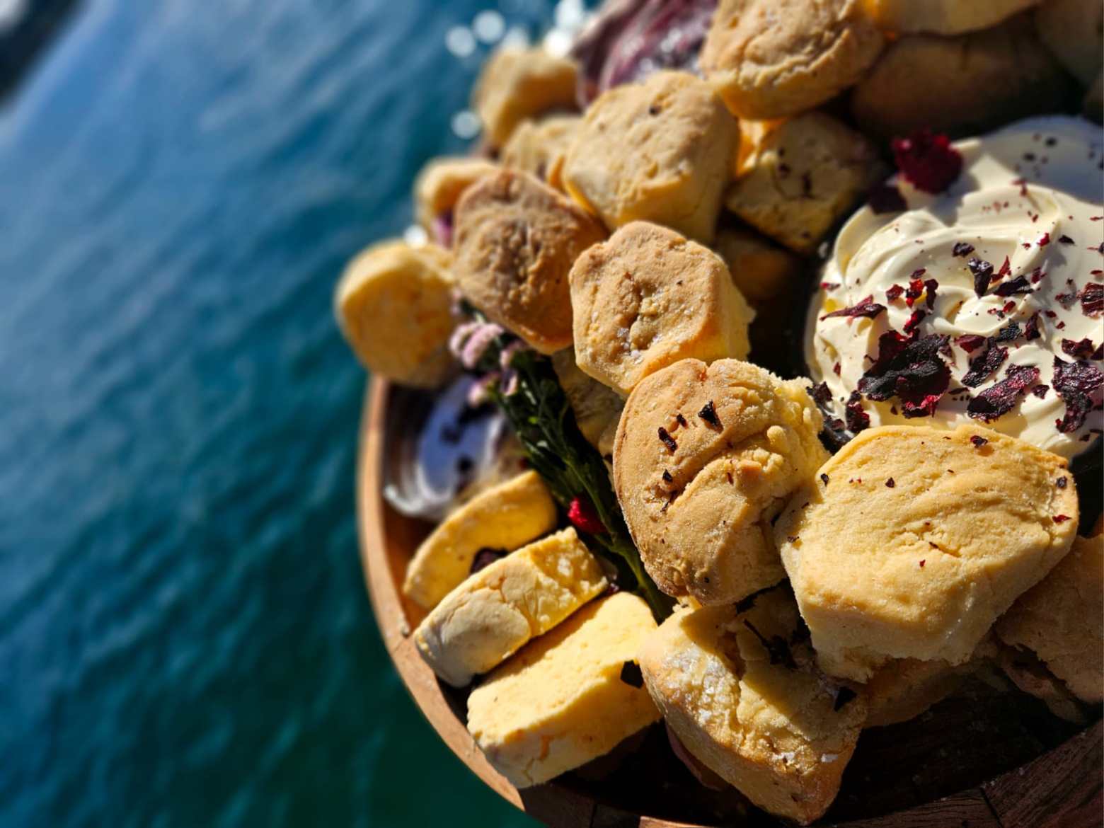 Close-up of scones with cream and dried rose petals by the water.