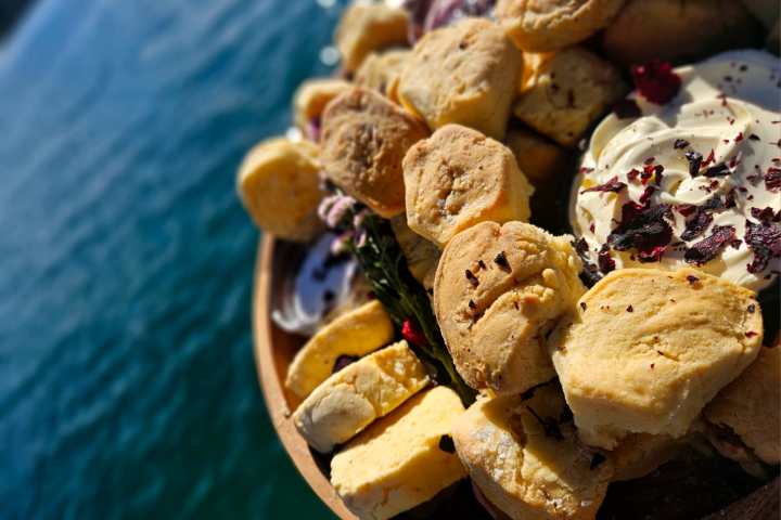 Close-up of scones with cream and dried rose petals by the water.