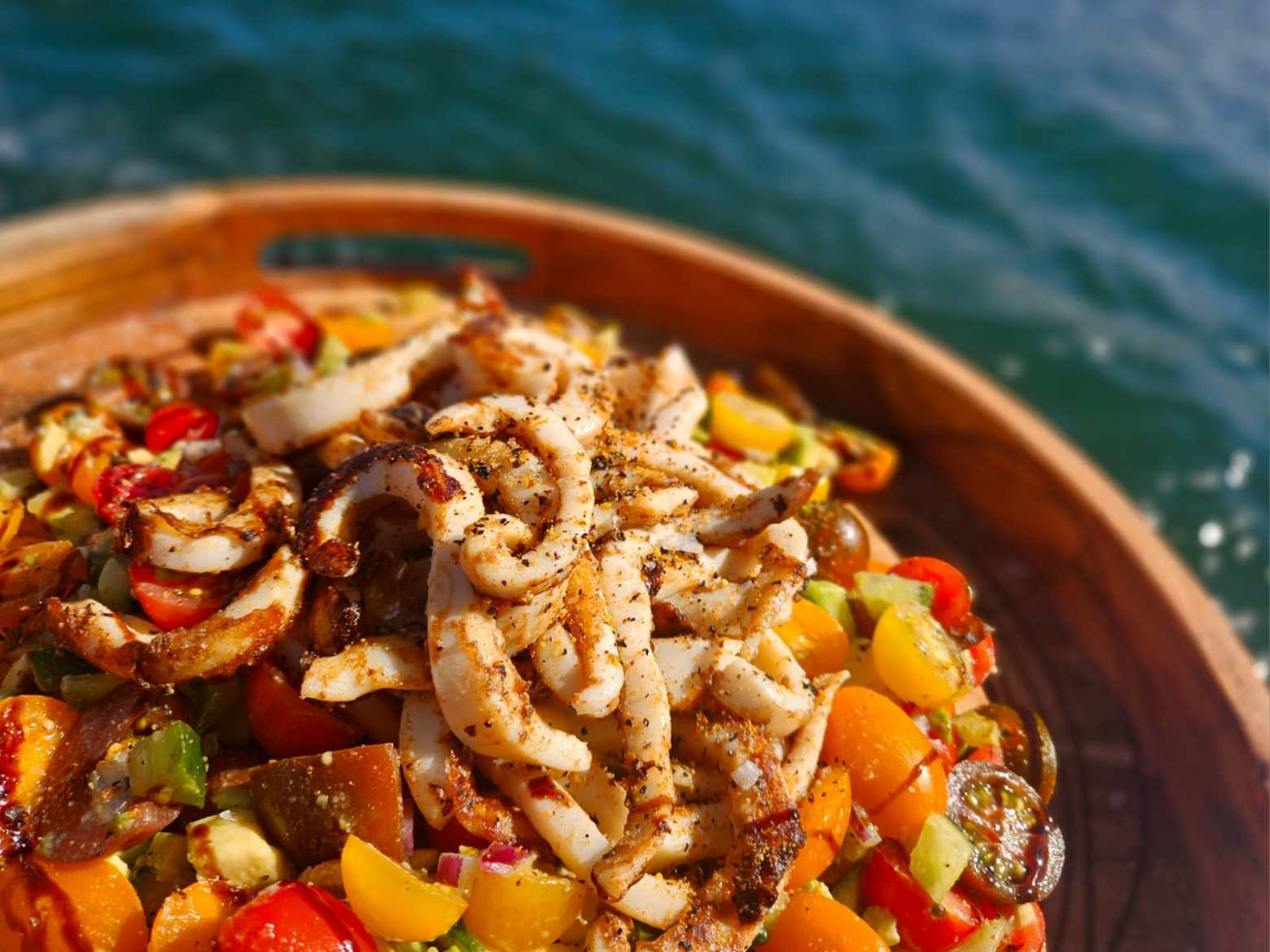 Grilled calamari on a colorful vegetable salad by the sea.
