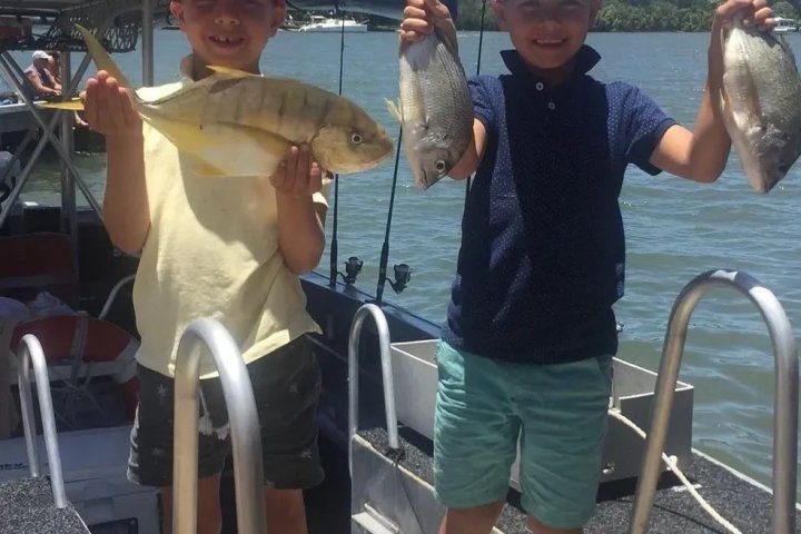 Two children on a boat holding up fish with smiles.